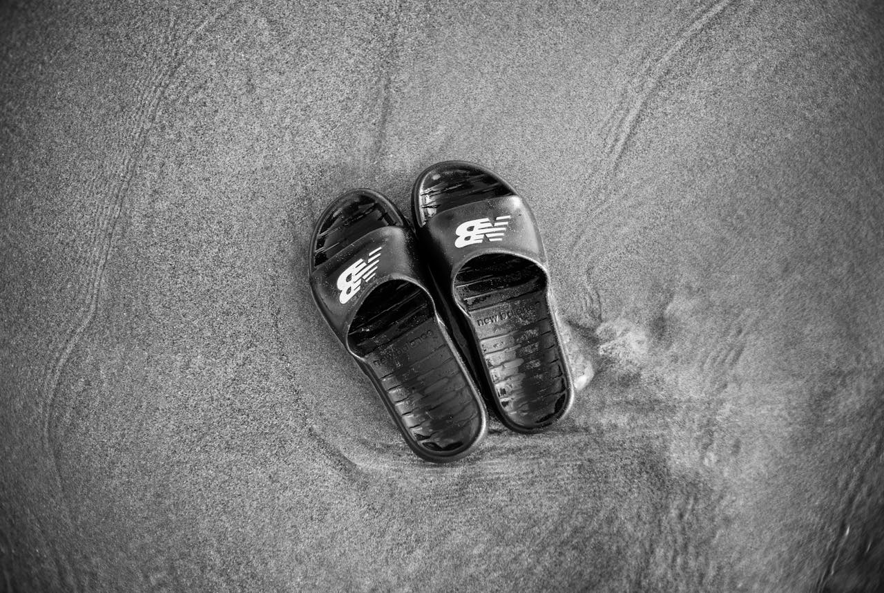 Black sandals on sand in a grayscale photo, capturing a minimalist and serene beach scene.